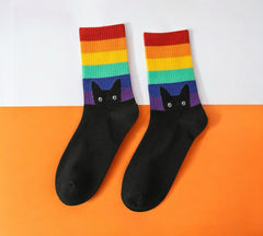 Peeking Cat Rainbow Pride Socks - Black color with rainbow stripes and black cat design, laid flat on orange and white background.