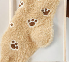 Cozy paw print socks laid on white bedding, highlighting their soft, fuzzy texture for ultimate comfort.