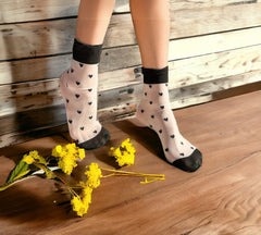 Heart-patterned sheer socks with black hearts, charming and playful gift socks for Valentine's Day, styled with yellow flowers on a wooden floor.