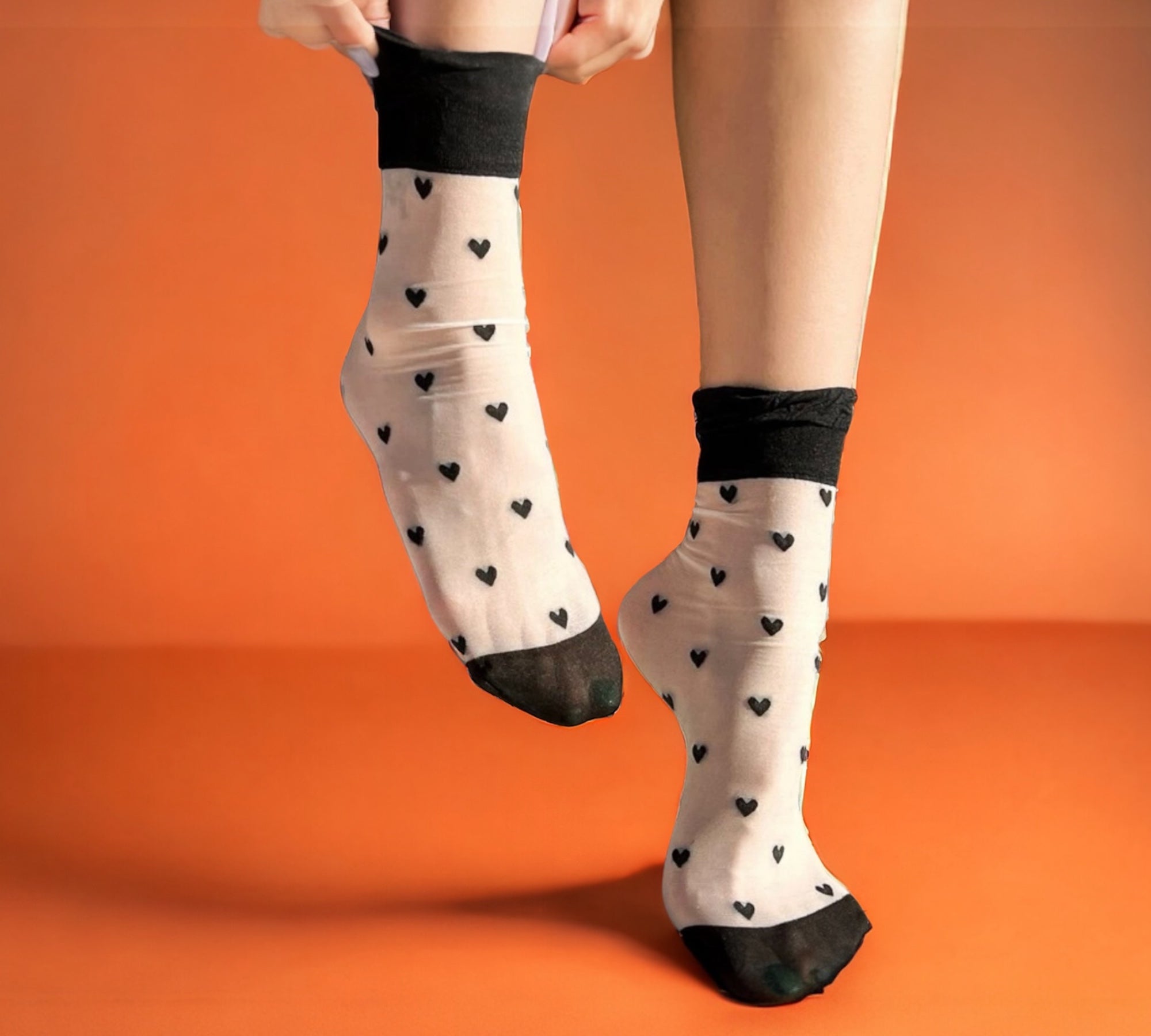 Stylish sheer crew socks with black heart patterns, perfect as romantic gift socks for Valentine's Day, styled on an orange background.