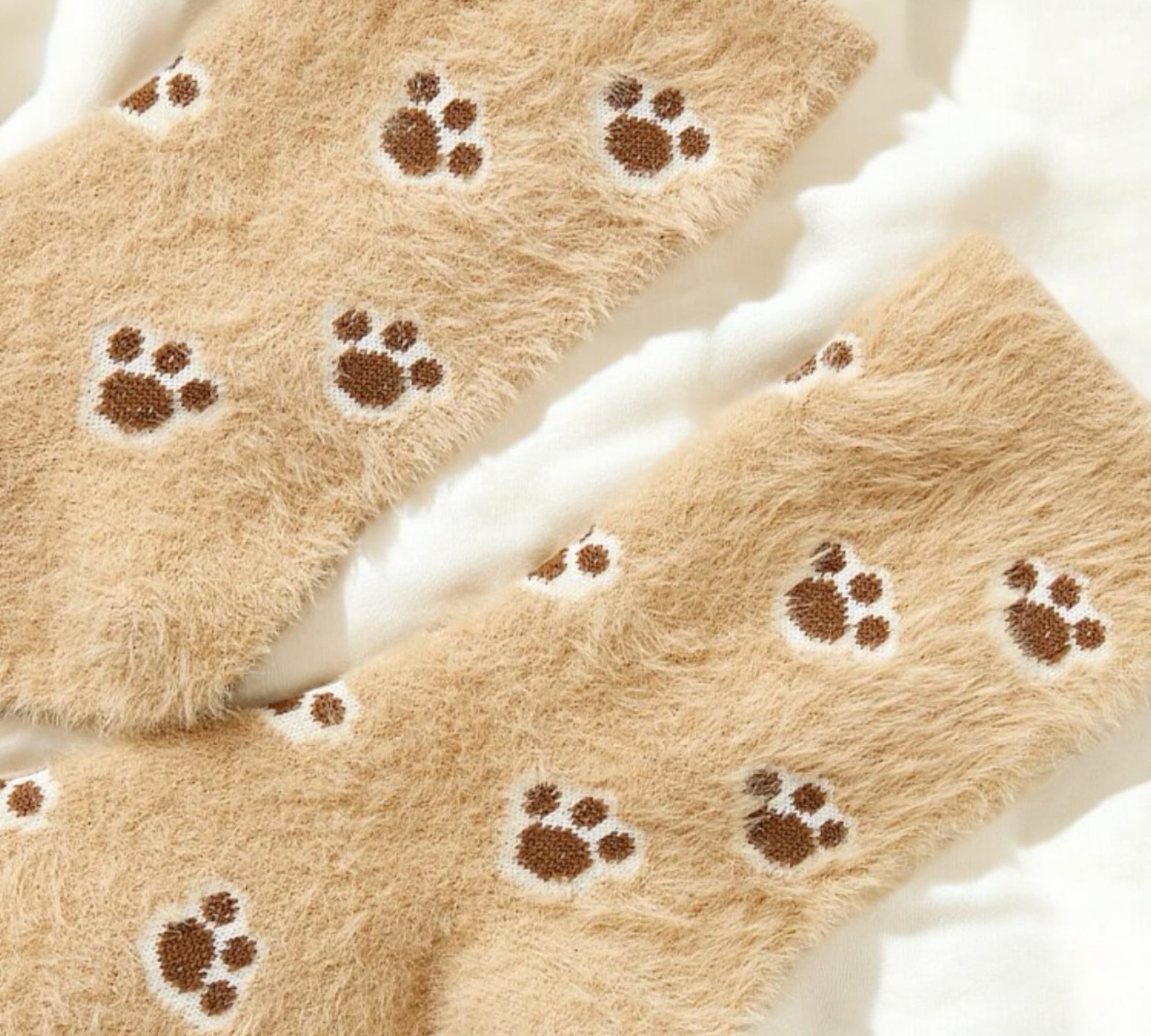 Detailed close-up of soft, fuzzy beige socks featuring a cute paw print pattern, ideal for cat and dog enthusiasts.