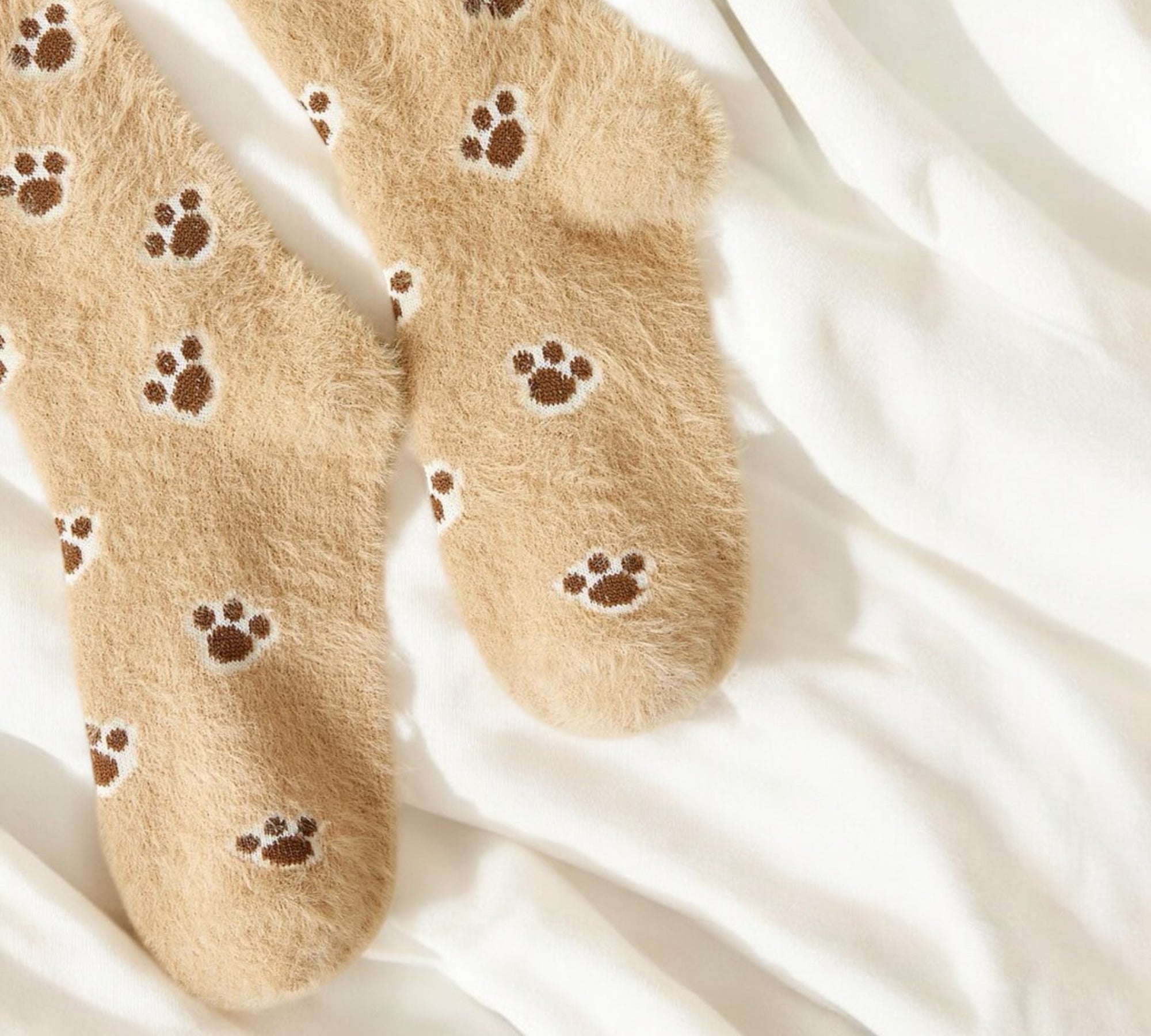 Fluffy beige socks with brown paw prints, shown on a stylish display for pet-themed loungewear.