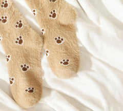 Fluffy beige socks with brown paw prints, shown on a stylish display for pet-themed loungewear.