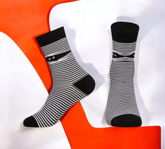 Black-and-white striped Halloween Mummy Socks featuring a playful peeking mummy design, laid flat on an orange and white backdrop.