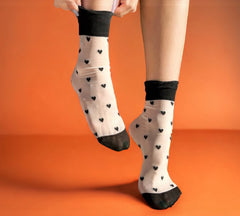 Stylish sheer crew socks with black heart patterns, perfect as romantic gift socks for Valentine's Day, styled on an orange background.